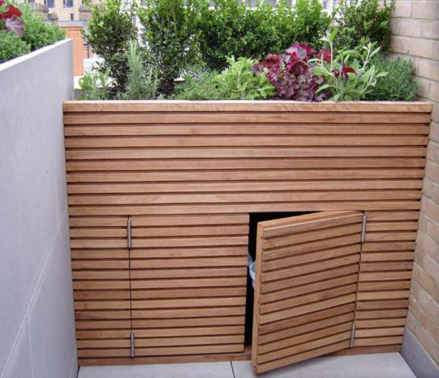 Stylish slatted wooden bin storage in a small garden with a green roof.