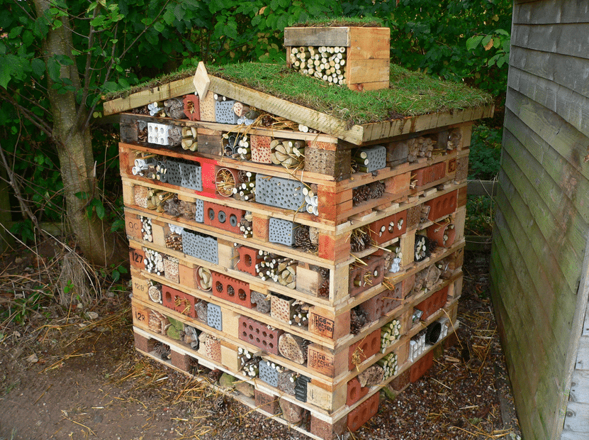 A bug hotel made with pallets and bricks with a green roof.