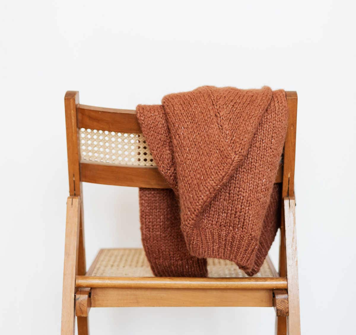 Rust coloured wool sweater on the back of a wooden chair.