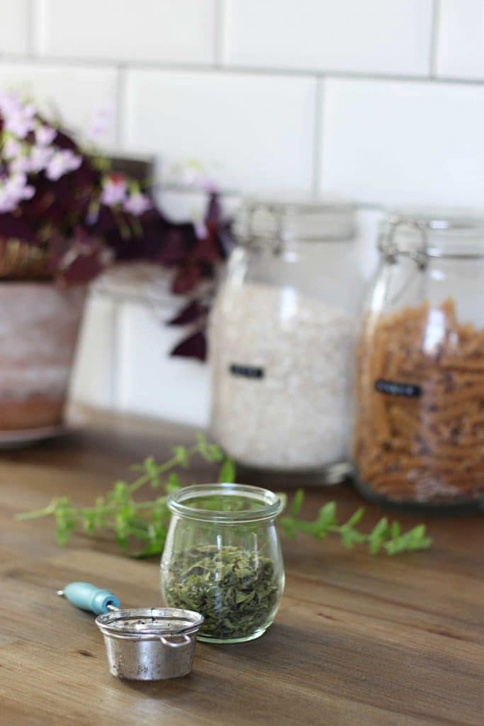 A jar containing dried lemon balm leaves next to a tea strainer