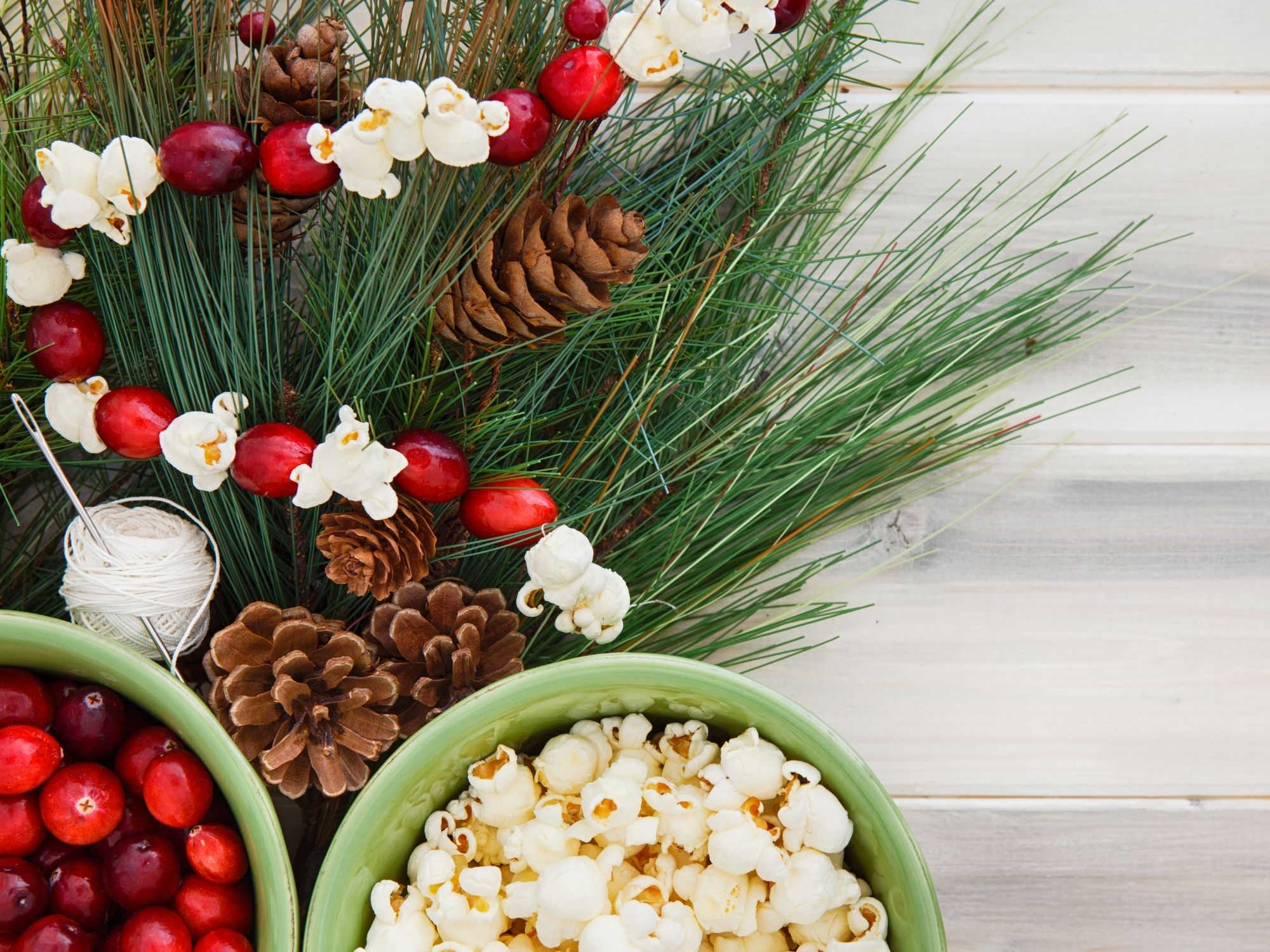 bowls of popcorn and cranberries, next to springs of pine, and a garland in process.