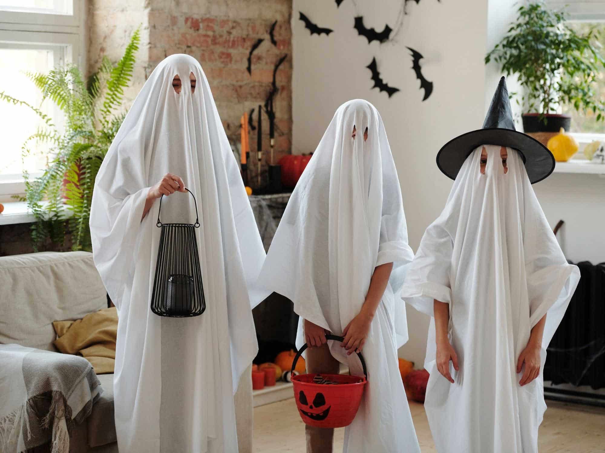 Three kids dressed as Halloween ghosts