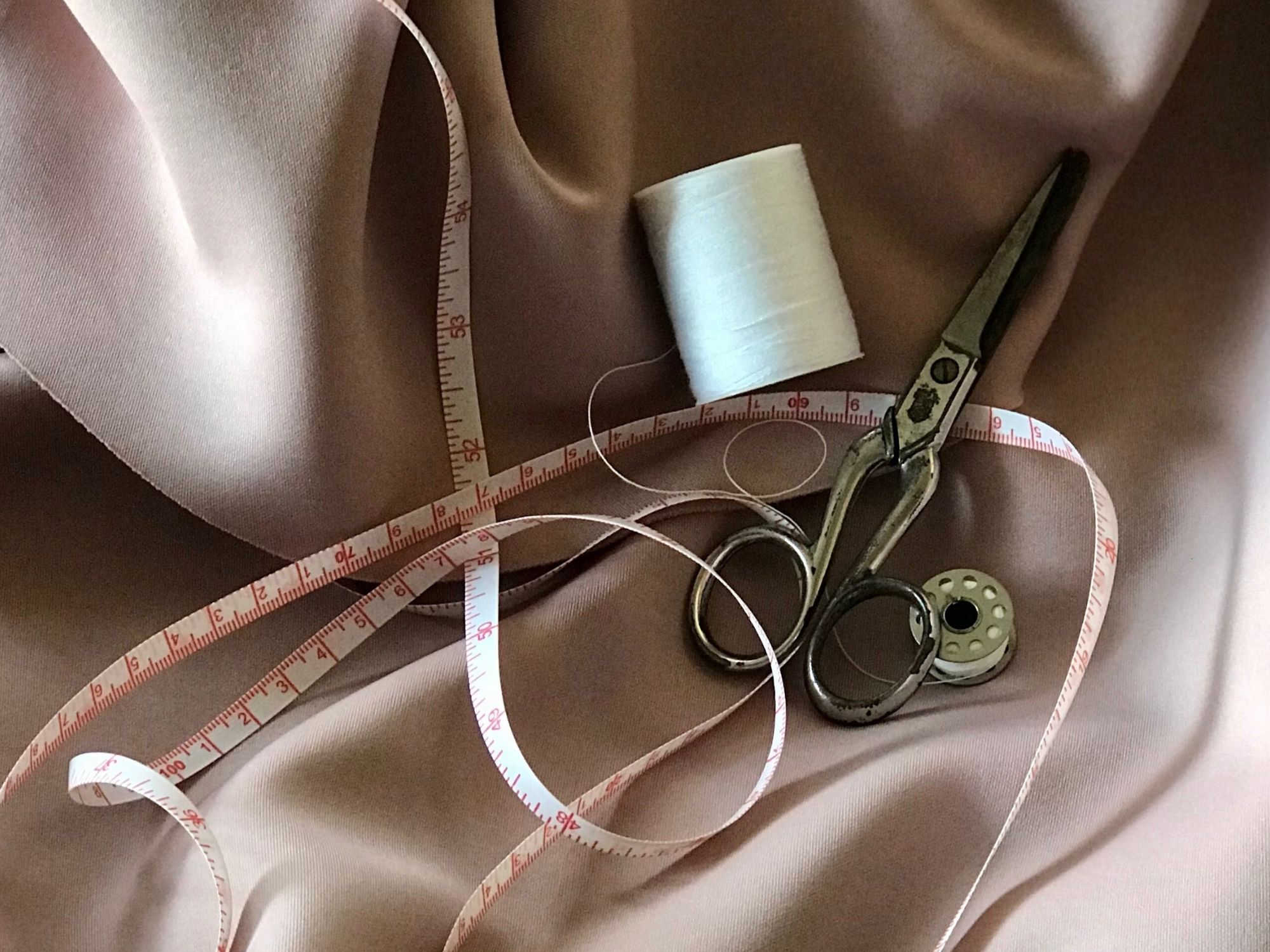 Scissors, measuring tape and thread on pink fabric