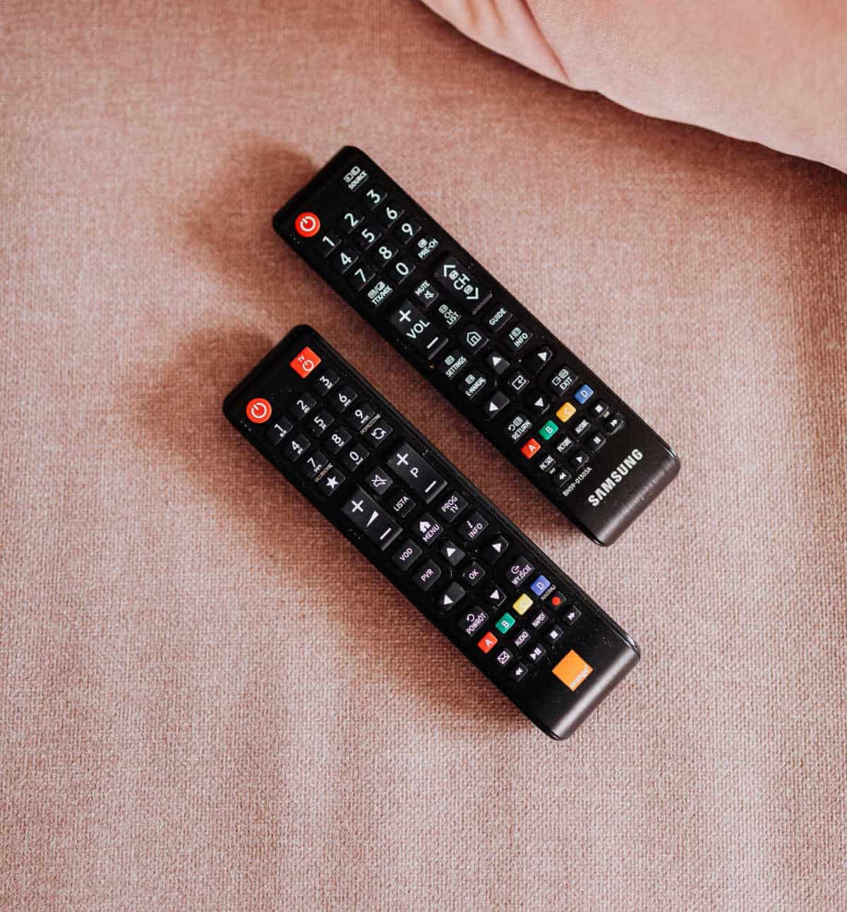 Two TV remote controls on a pink sofa
