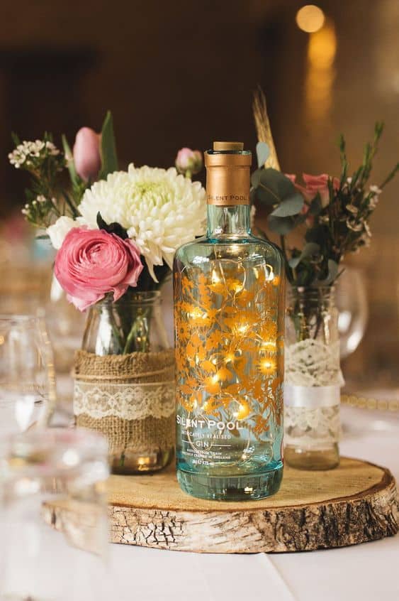 Spirit bottle filled with LED lights on a table with vases of flowers.