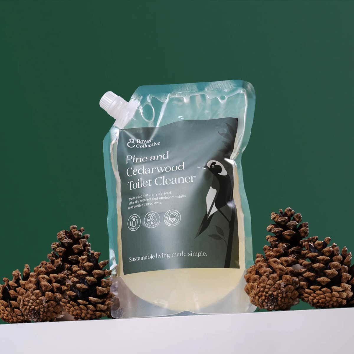 Refill pouch of pine and cedarwood toilet cleaner from Bower Collective on surrounded by pine cones and on a green background.