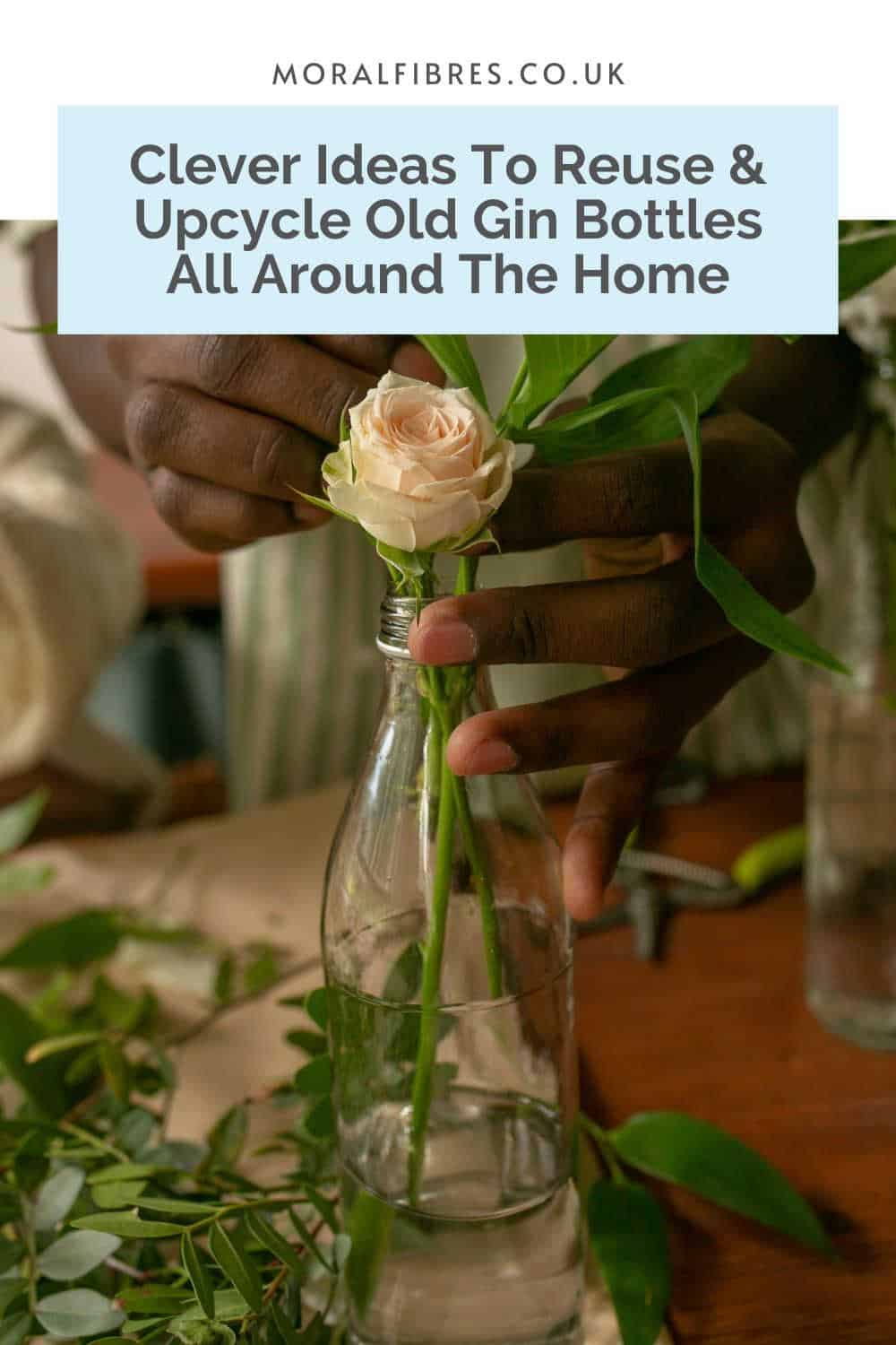 Person using an old bottle as a vase for a cream rose and foliage, with a blue text box that reads clever ideas to reuse and upcycle old gin bottles.