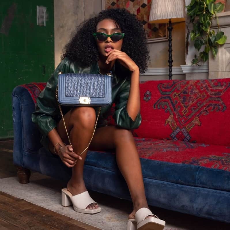 Person sitting on a red sofa, holding a navy vegan handbag from black-owned ethical fashion brand Amschela.