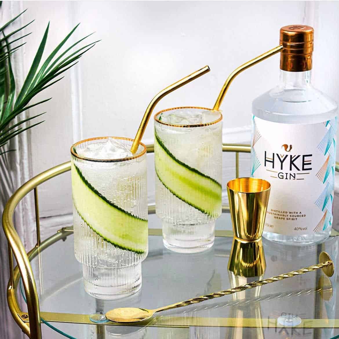 Bottle of Hyke gin next to two tall glasses of gin with cucumber in them.