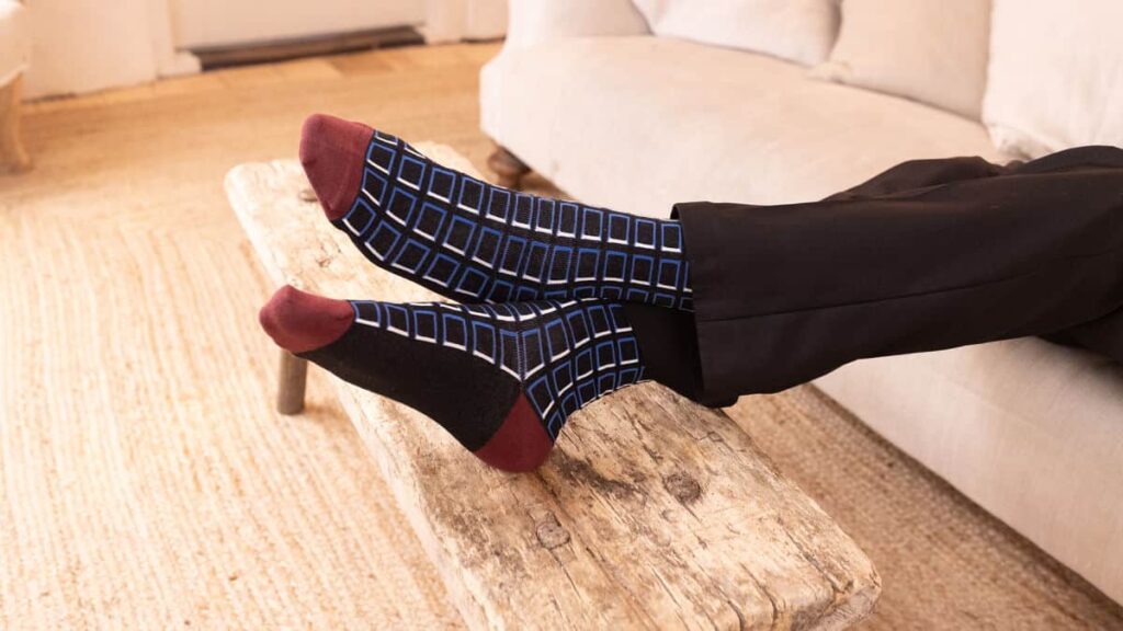 Person with feet up on wooden bench wearing navy cube print socks.