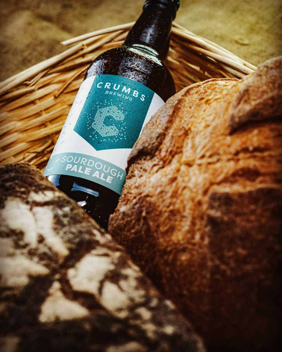 Bottle of Crumbs Brewing Sourdough Pale Ale nestled in a basket of bread.